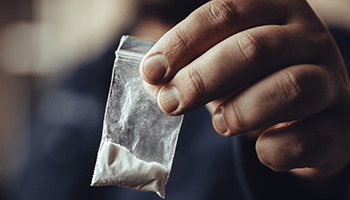 closeup view of a hand holding small bag with a white powder inside, representing drug charges